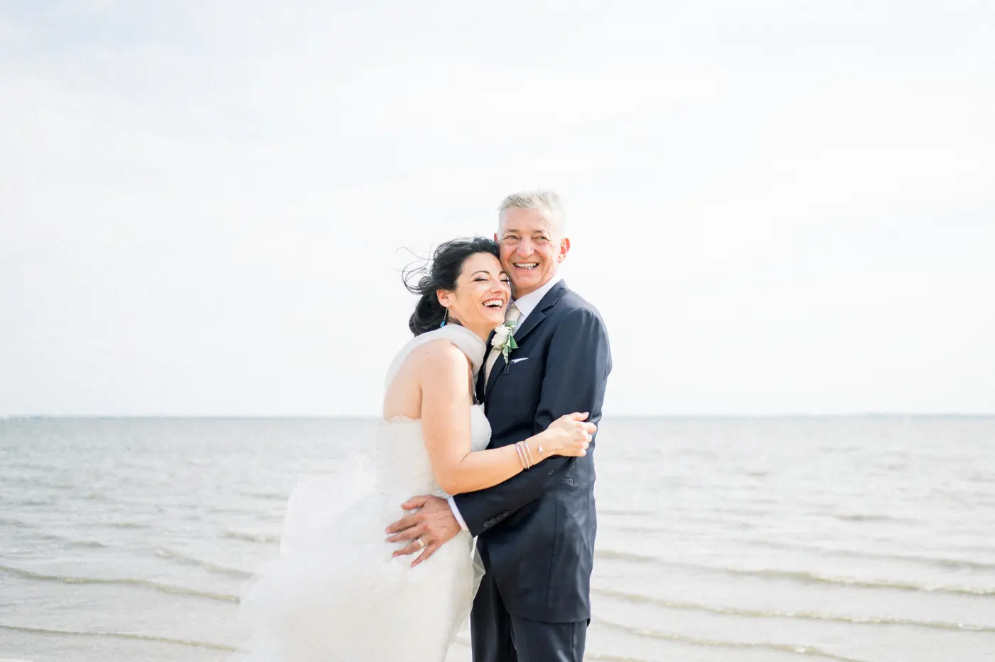 The bride and groom in a close embrace on the beach facing Arcachon Bay