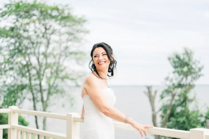 The bride smiling as she leans on the white railing above the bay