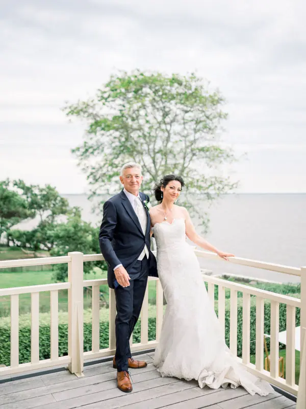 The bride and groom hand in hand on the terrace above the bay