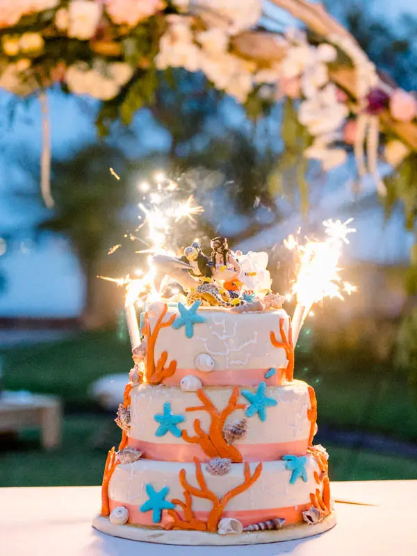 Wedding cake decorated with orange coral and starfish, topped with sparklers