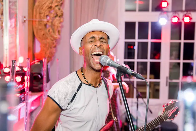 The band's singer in a white hat performing passionately at the party