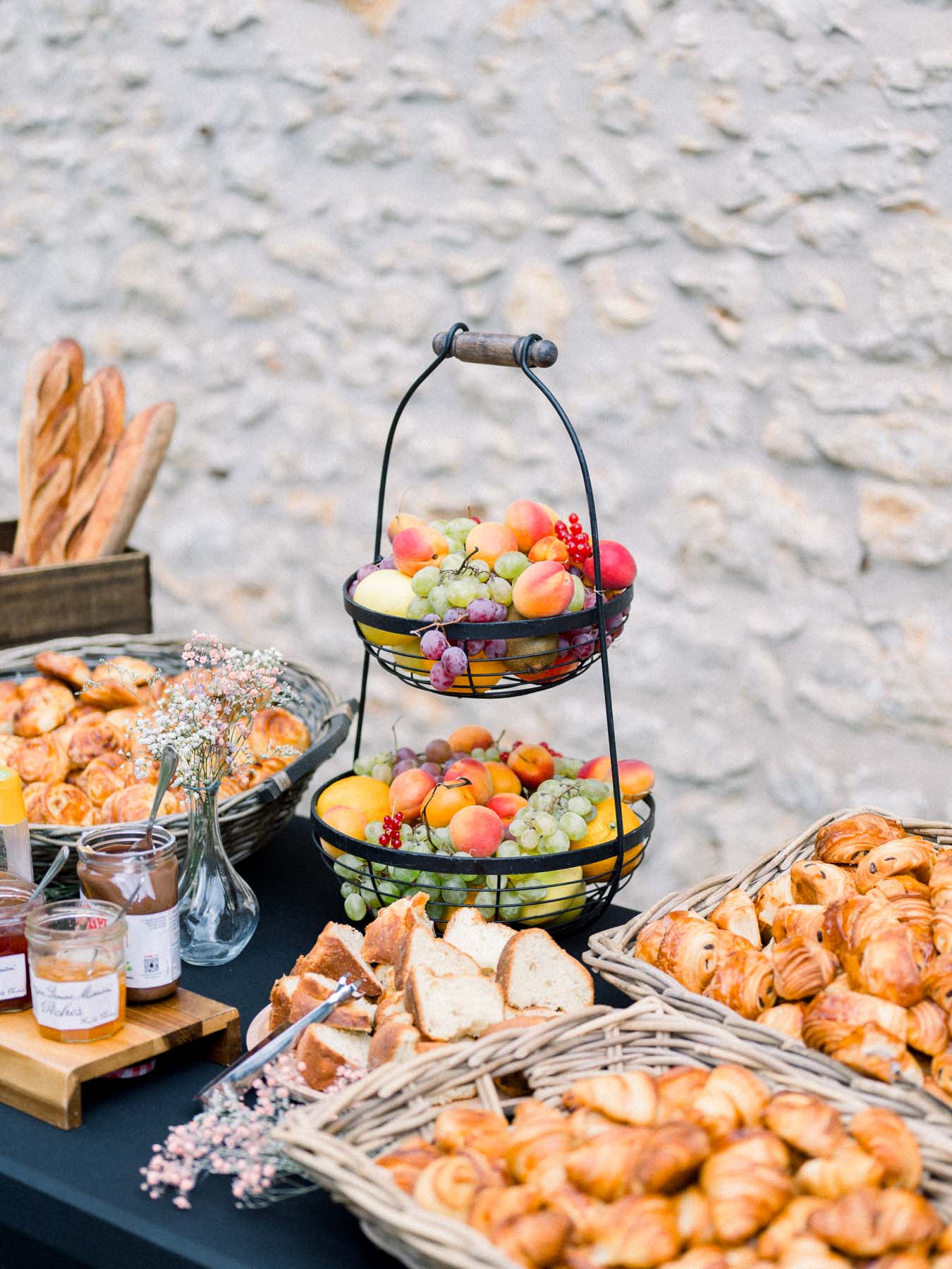 Brunch buffet with pastries and a fruit basket against a stone wall