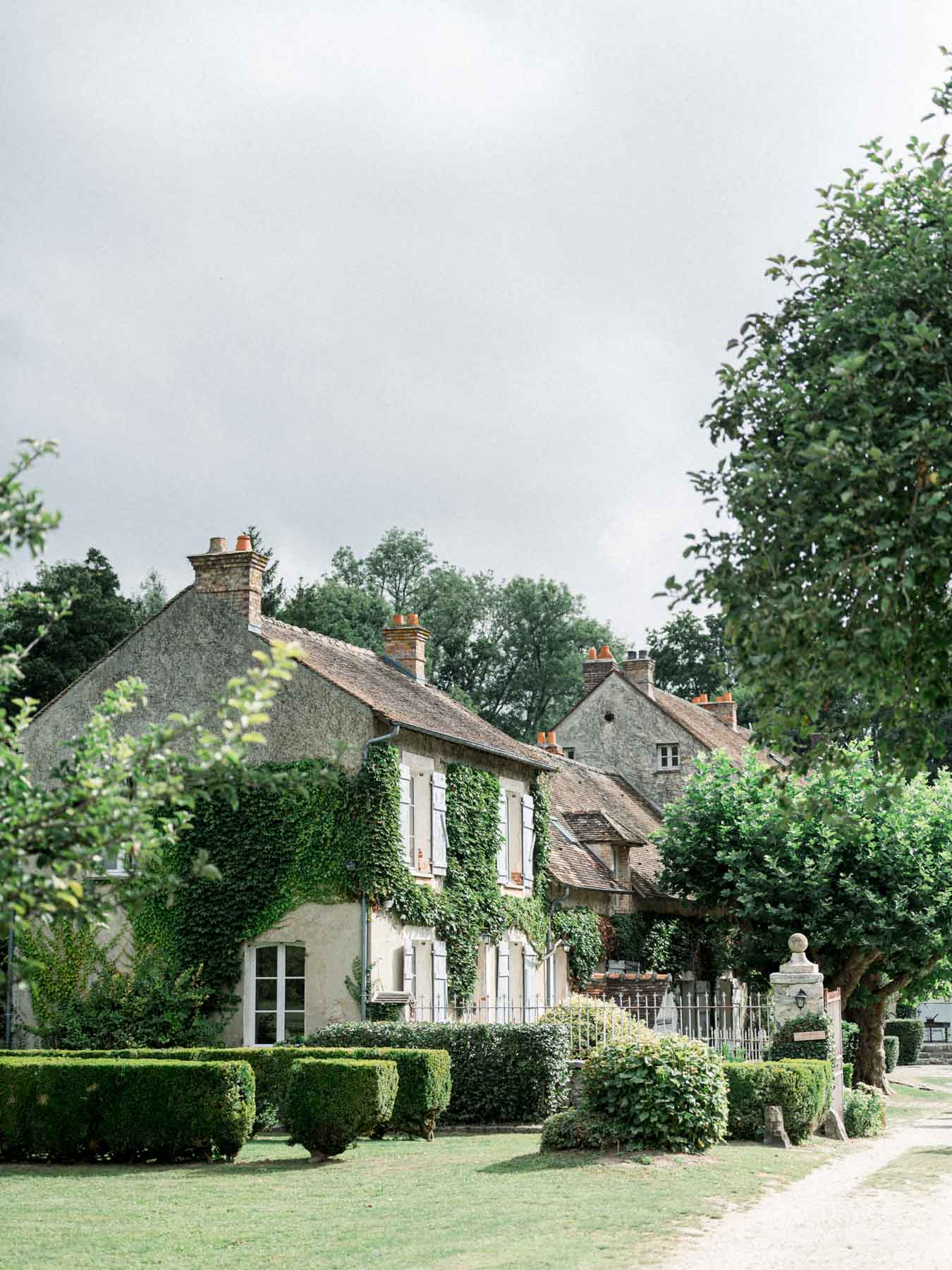 Stone houses and garden of the Moulin de Launoy hamlet under a cloudy sky