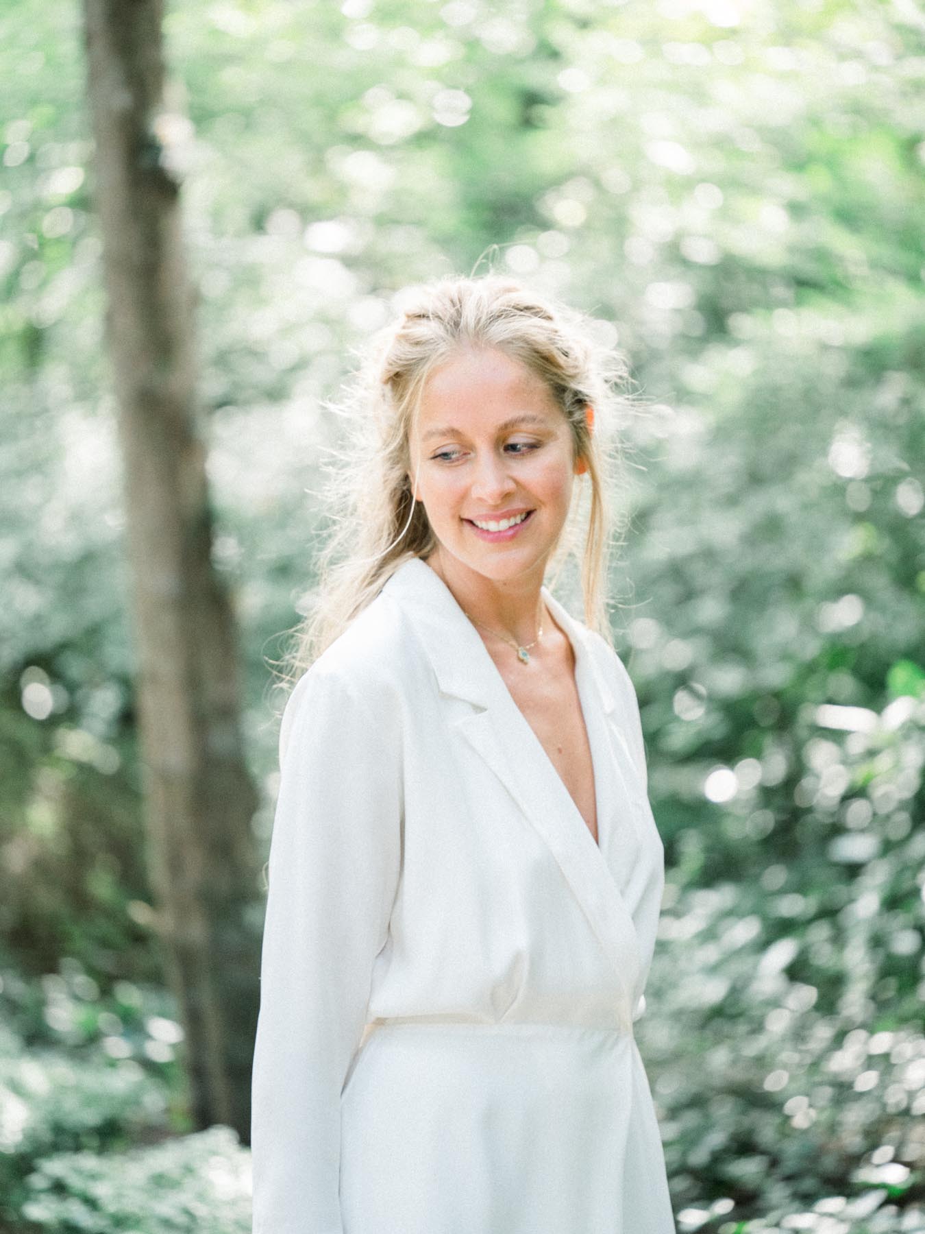 Smiling bride in a white suit among the trees of Parc de Bagatelle, Paris