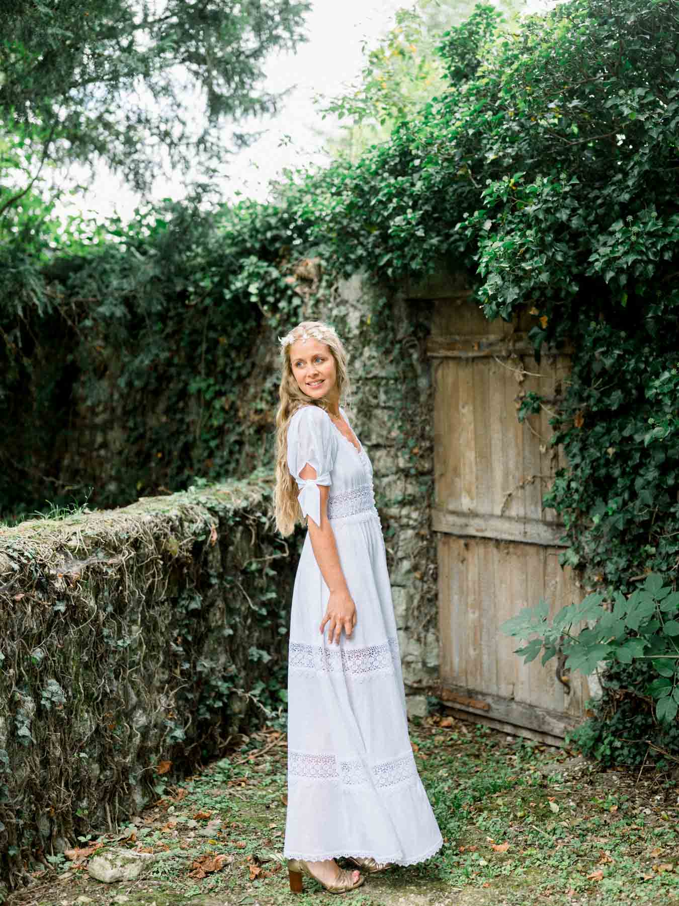 The bride in a boho dress by an old ivy-covered wooden gate