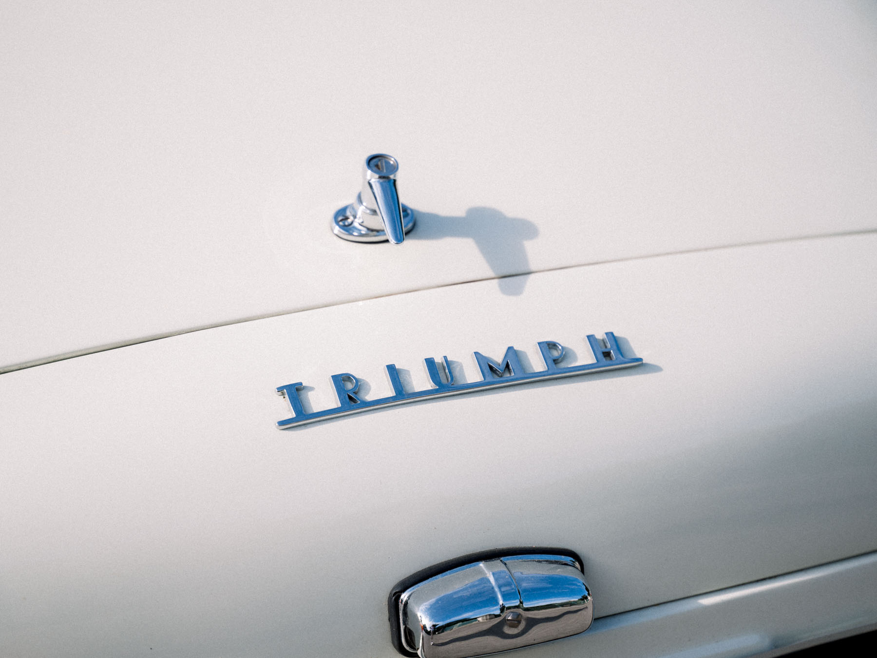 Chrome Triumph badge on the white bonnet of the couple's vintage car
