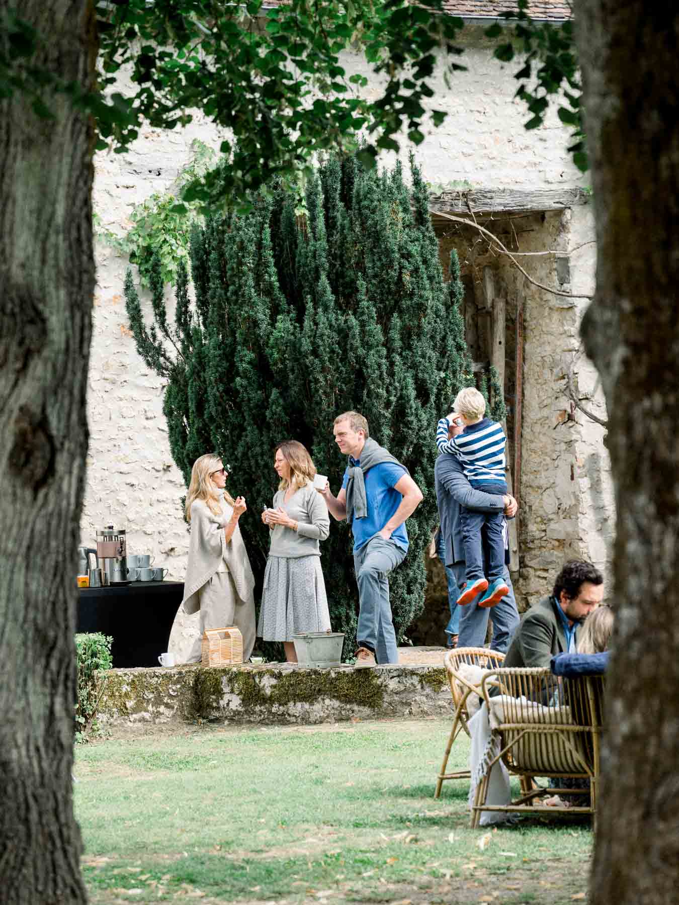 Guests chatting in the stone courtyard during the brunch, seen through the trees
