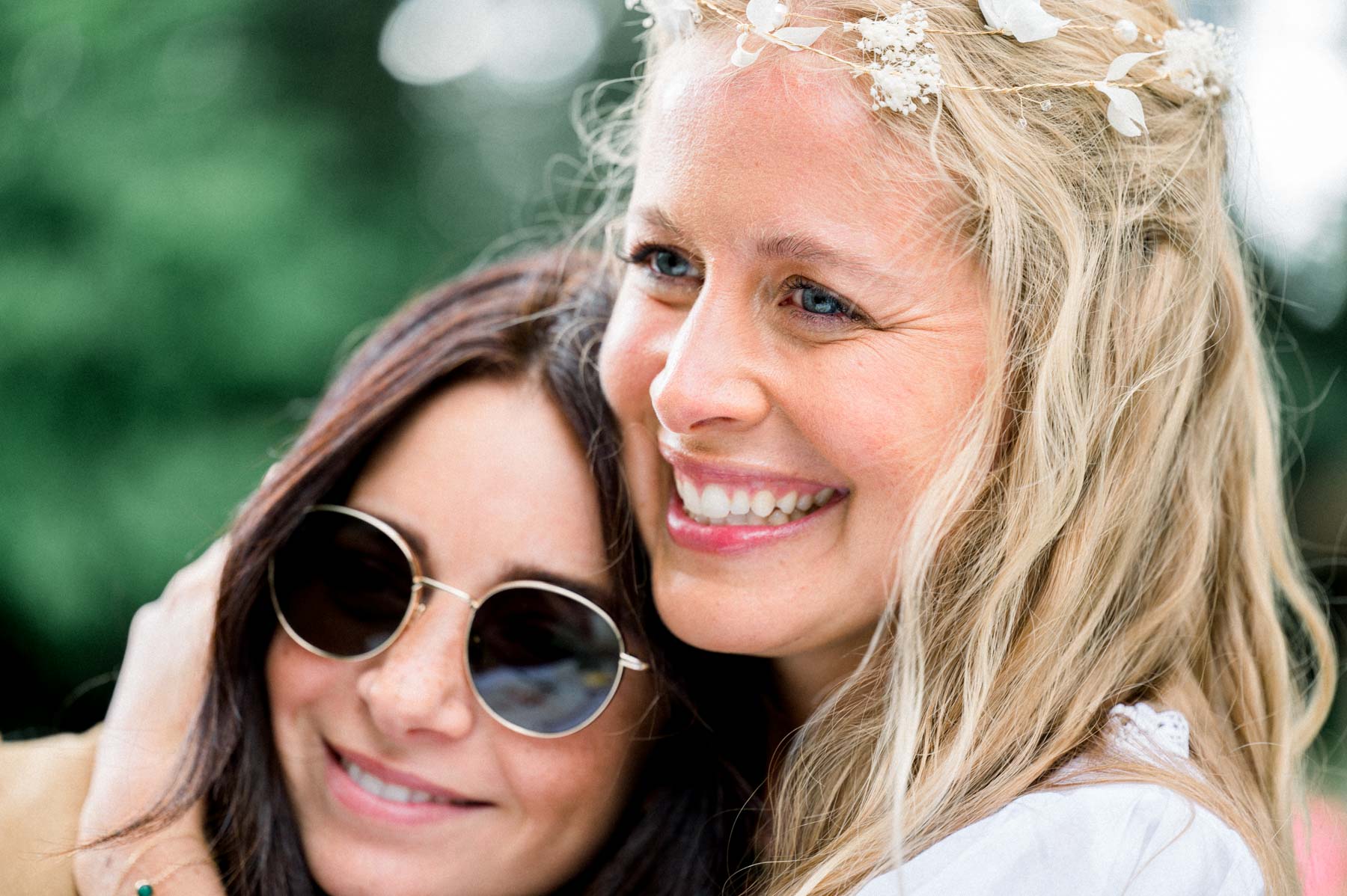 The bride cheek to cheek with a friend in sunglasses