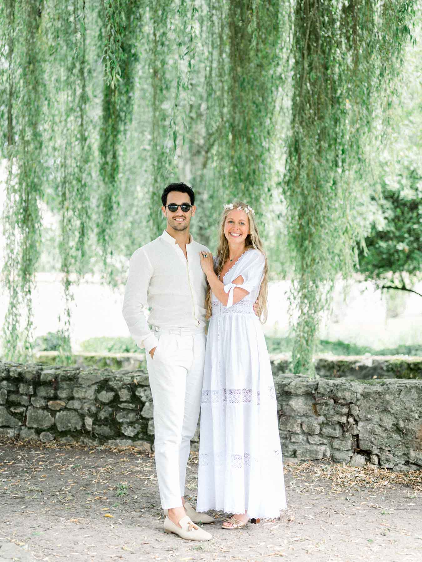 The bride in a boho dress posing with a loved one beneath a weeping willow