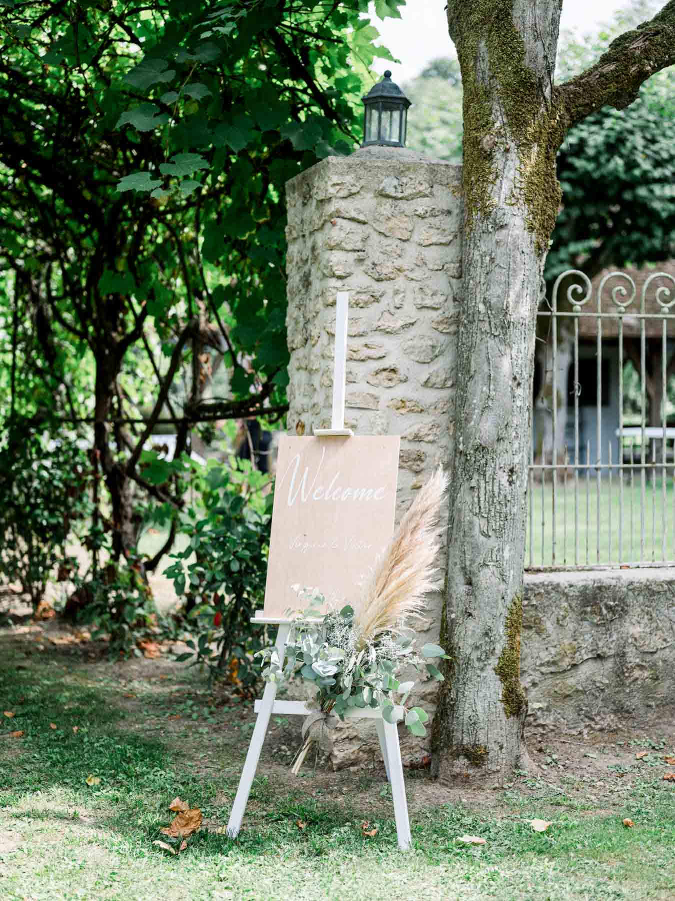 Welcome sign on an easel decorated with dried flowers beside a stone pillar
