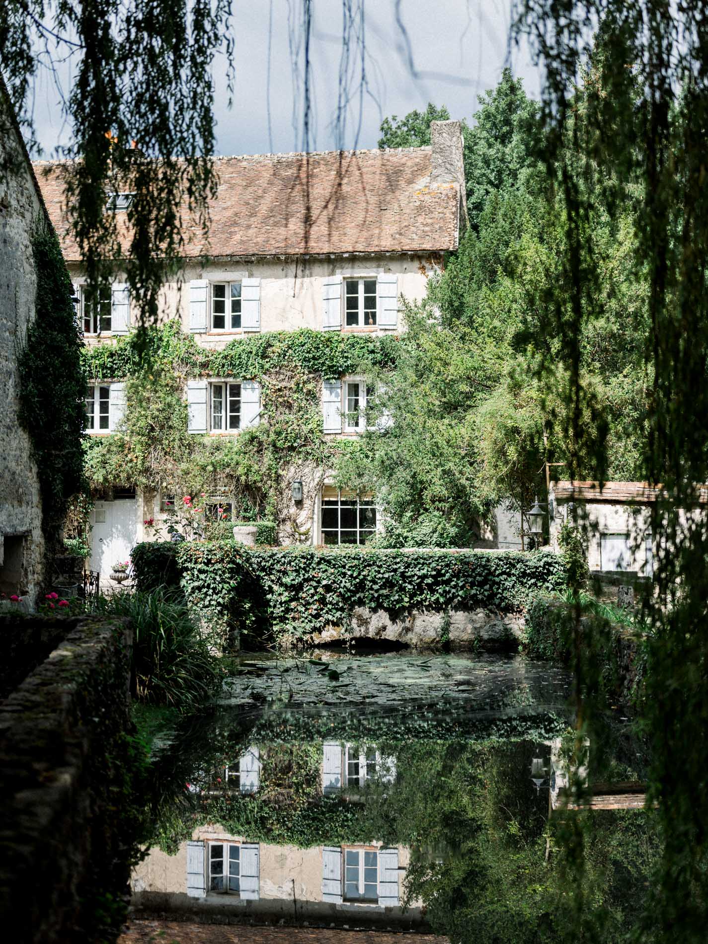 The ivy-clad mill reflected in the water between weeping willows