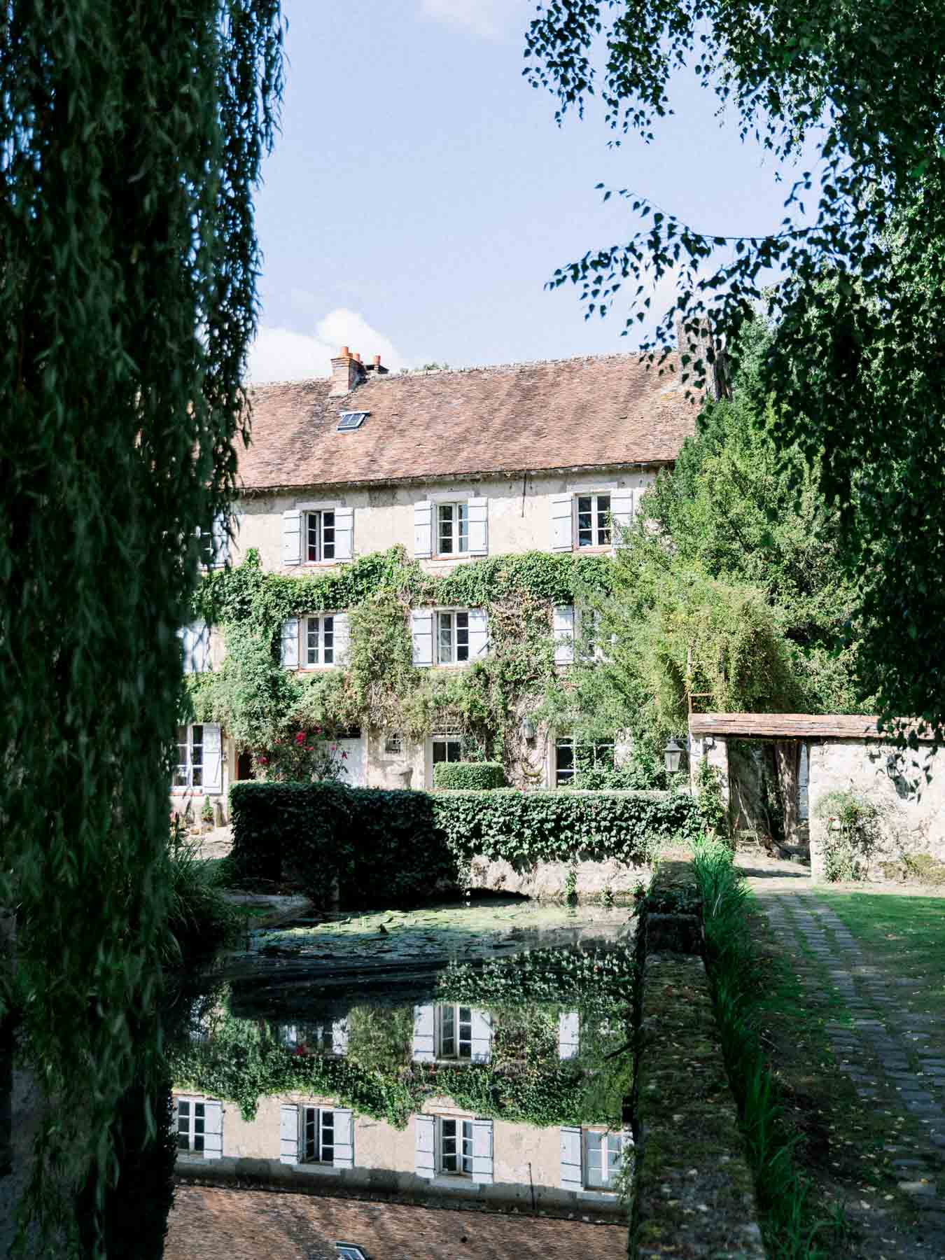 The mill house reflected in the water, framed by the garden greenery