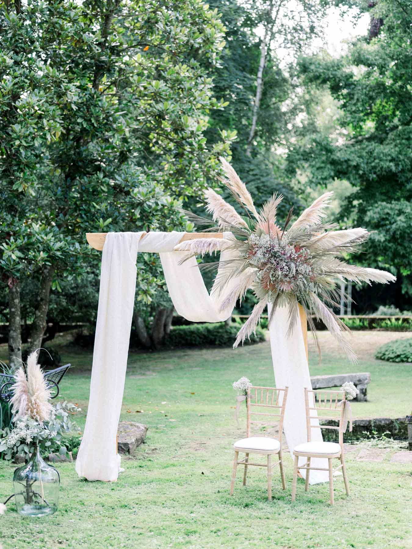 Ceremony arch in white fabric topped with a dried-flower arrangement