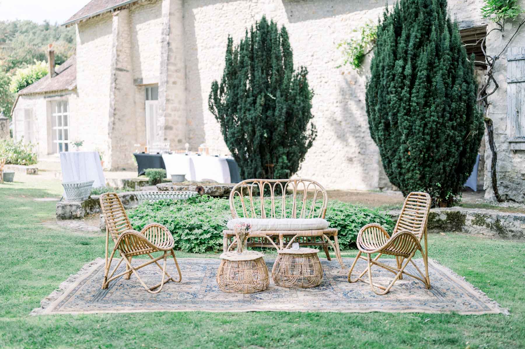 Rattan armchairs on a rug on the lawn in front of the stone houses