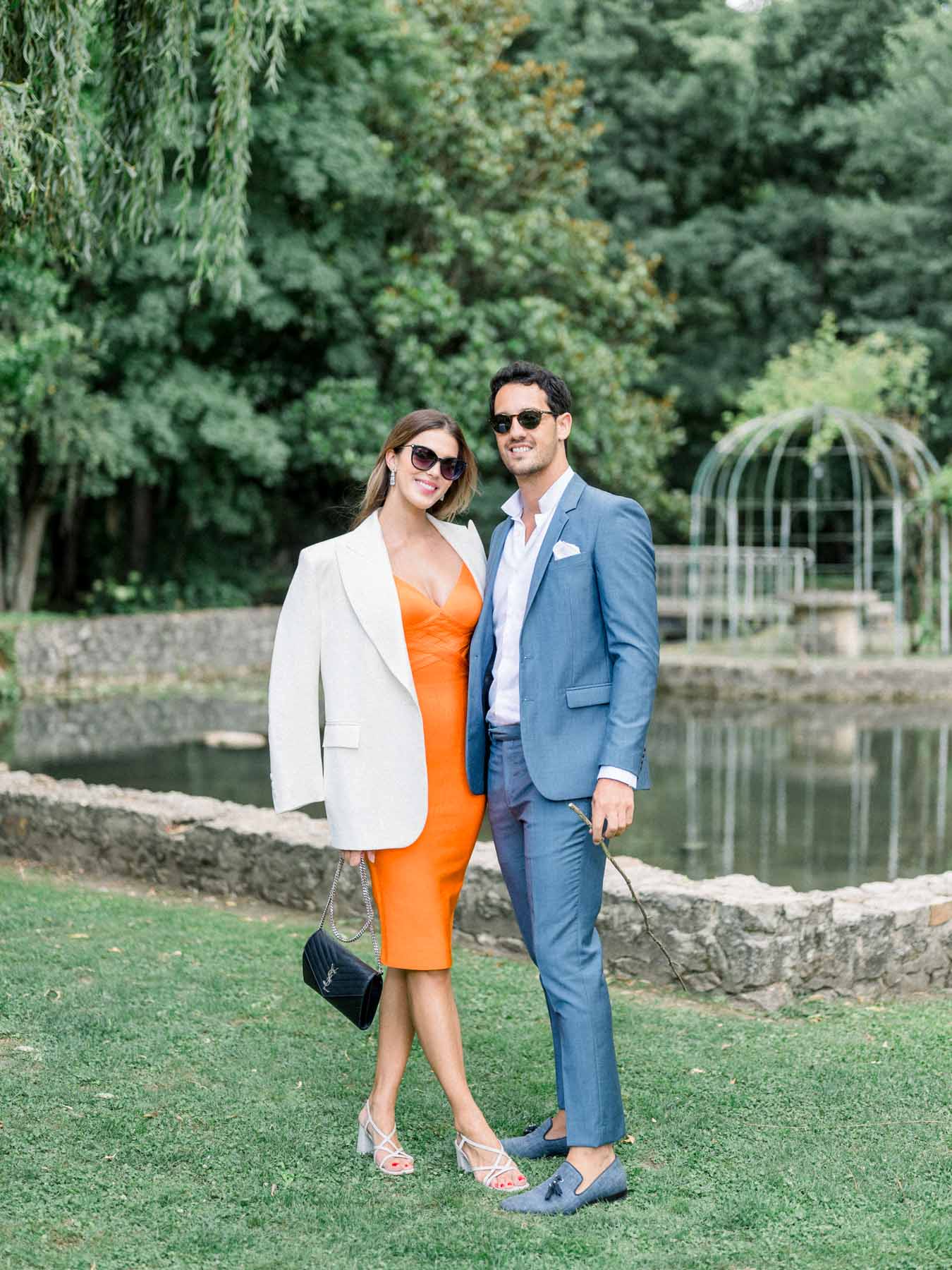 Elegantly dressed guests, orange dress and blue suit, by the pond