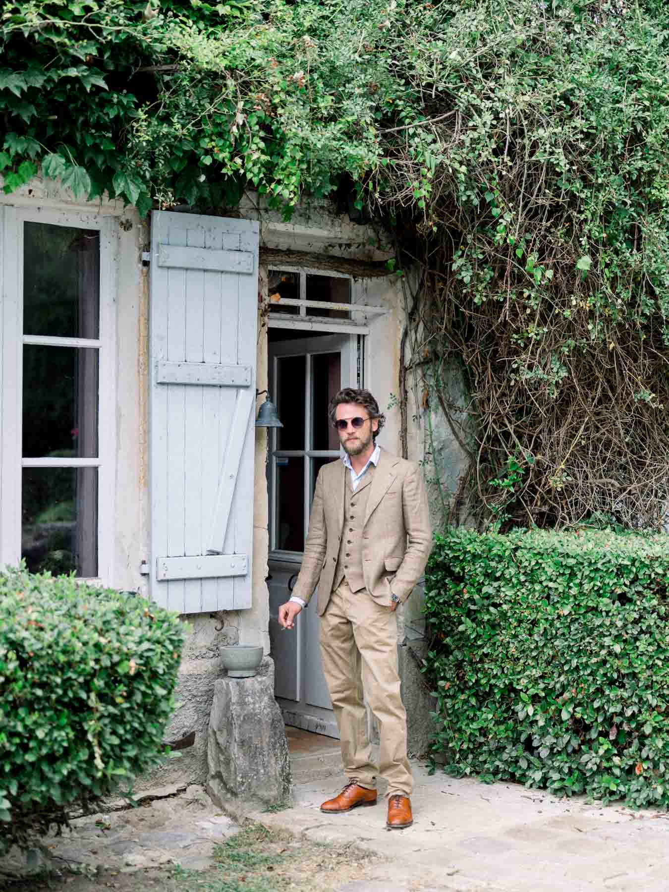 Guest in a beige suit and sunglasses at a doorway with grey shutters