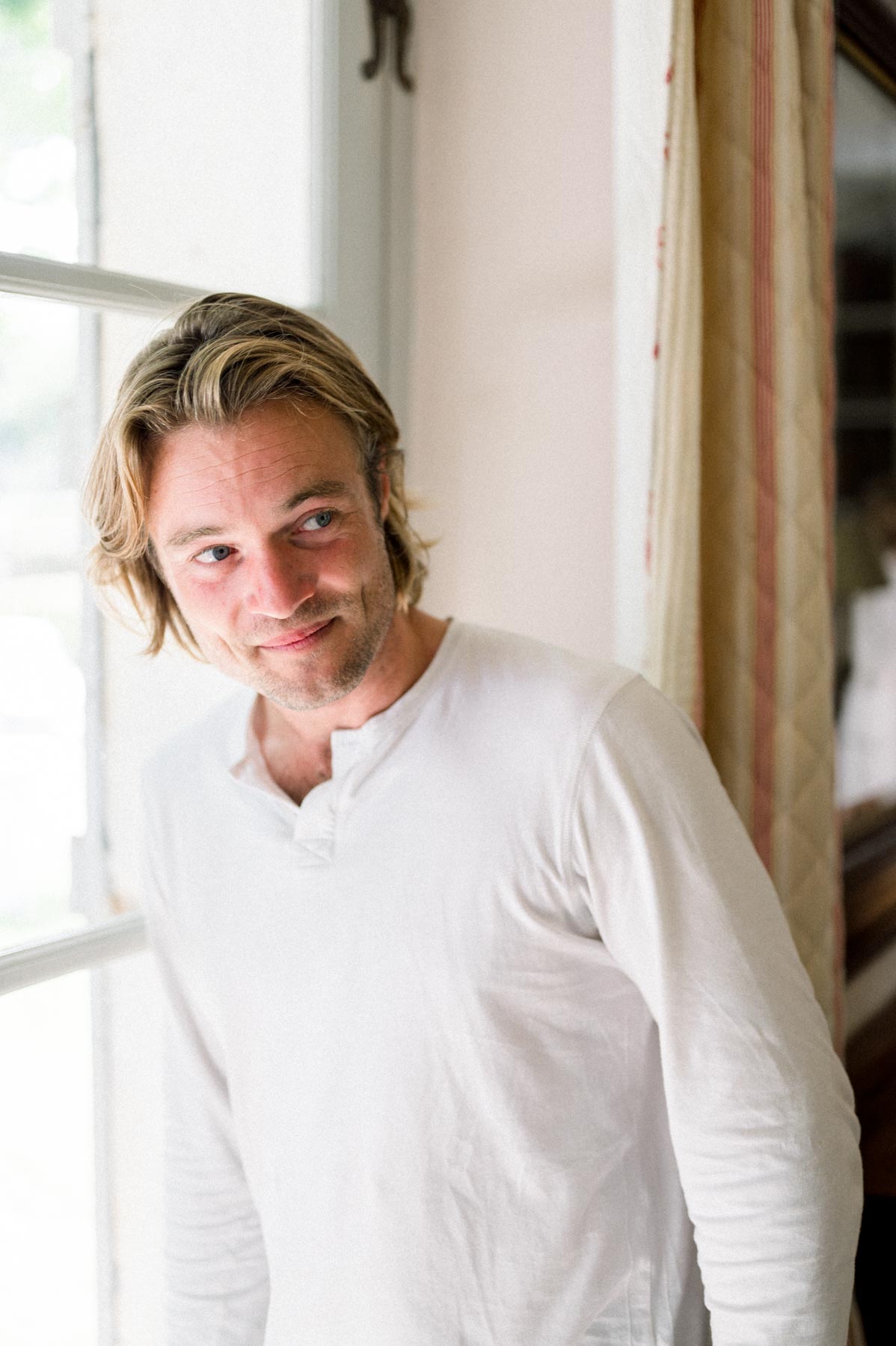 Portrait of the smiling groom in a white shirt by a window before the ceremony