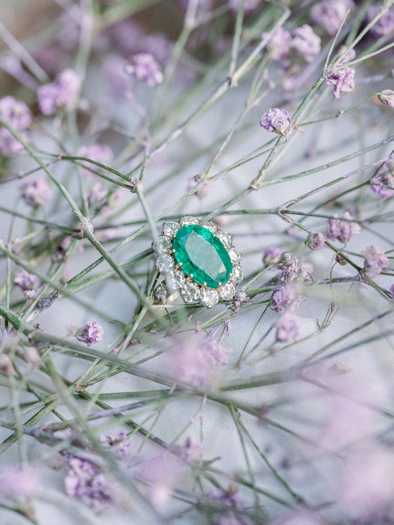 Emerald engagement ring resting among mauve gypsophila