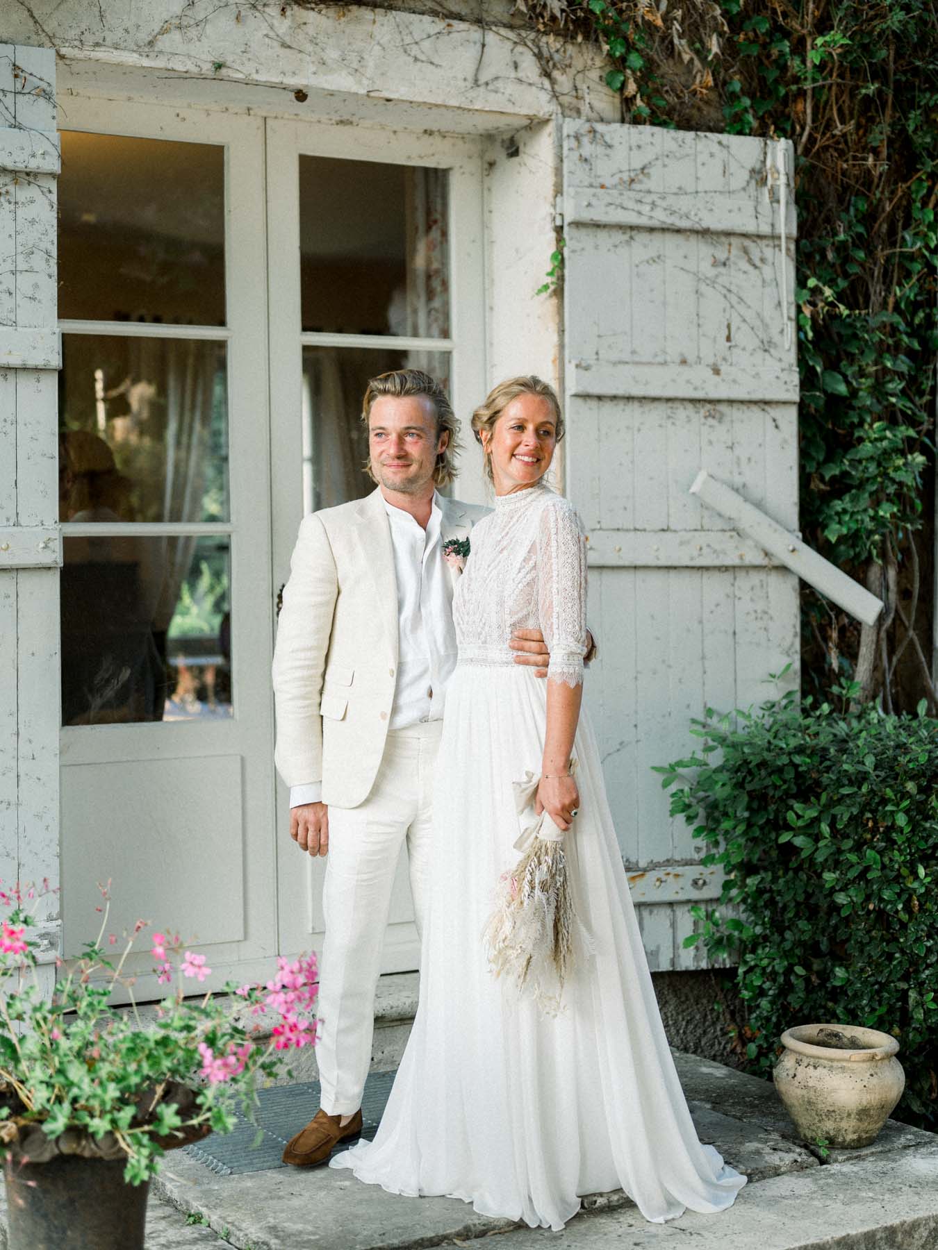 The couple on the doorstep of the stone house, surrounded by flowers