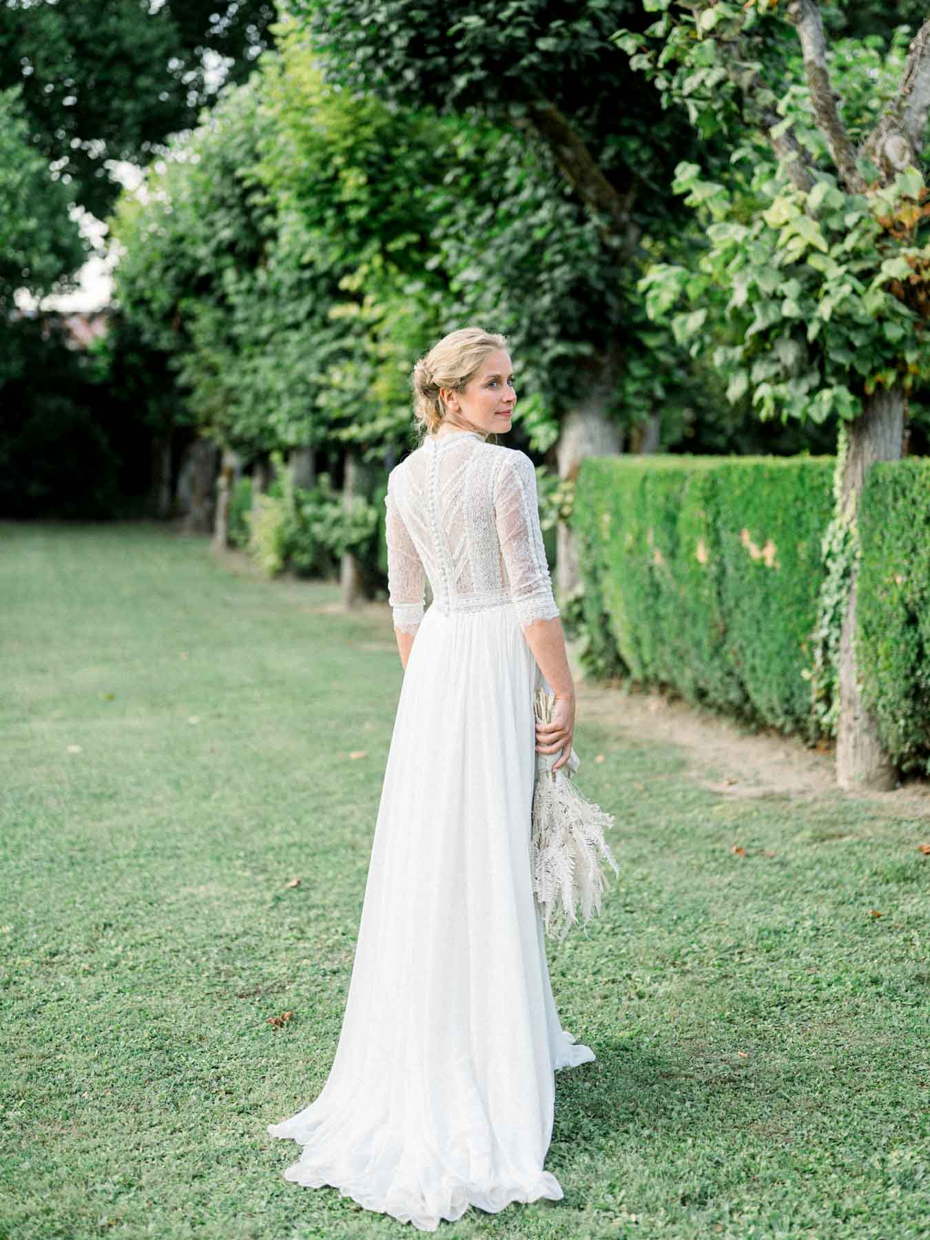 The bride glancing back over her shoulder, lace gown and dried-flower bouquet