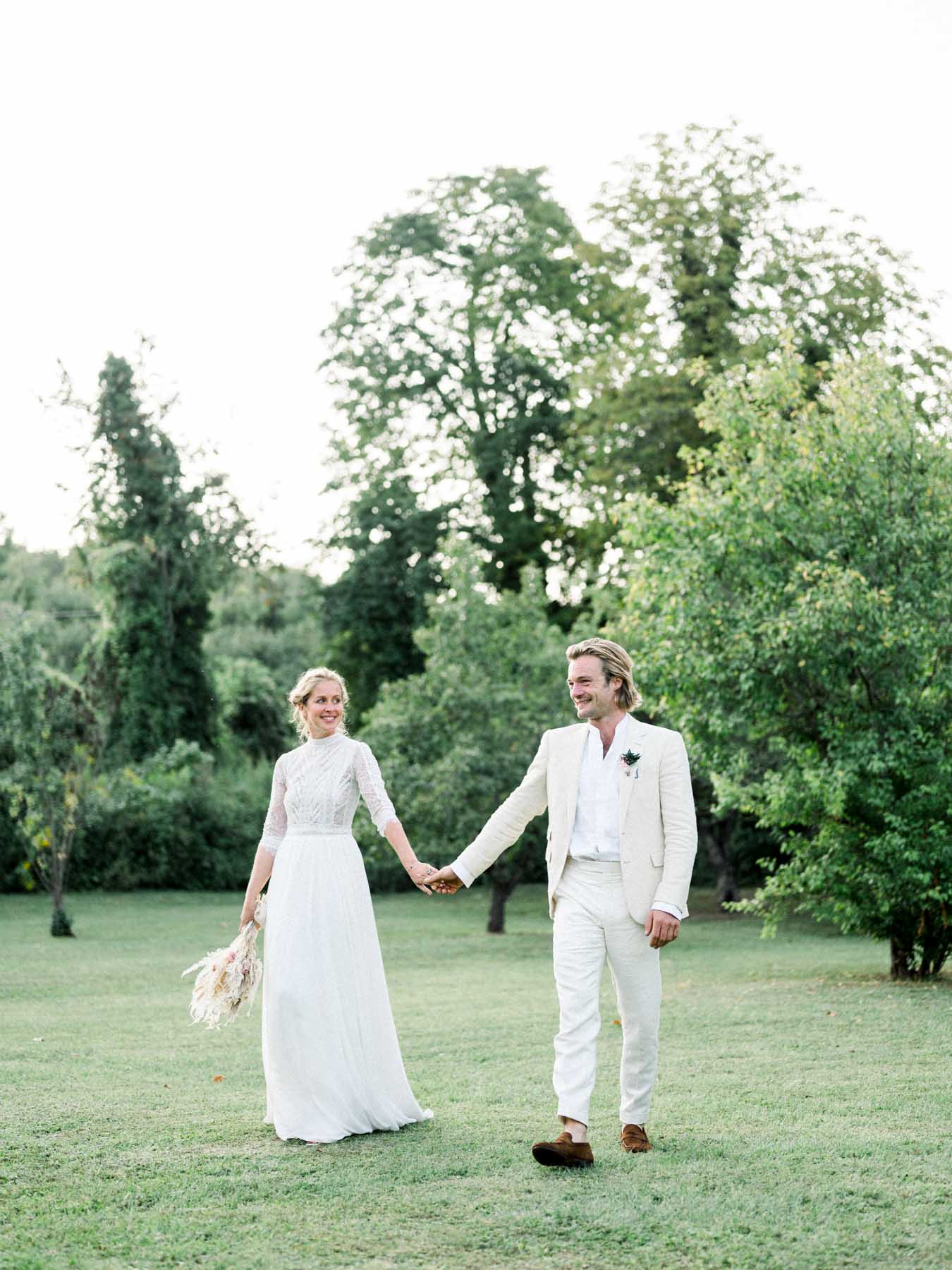 The couple walking hand in hand across the lawn at Moulin de Launoy