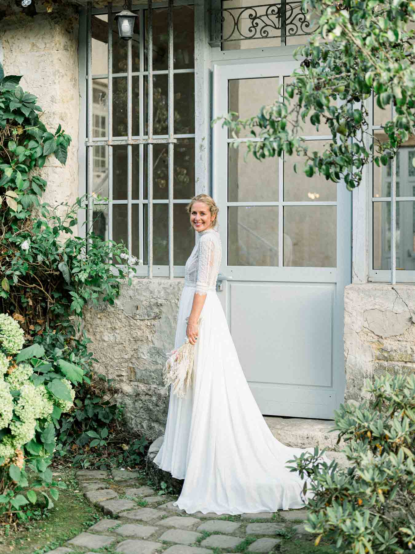 The bride before a glass door of the stone house, her train spread out