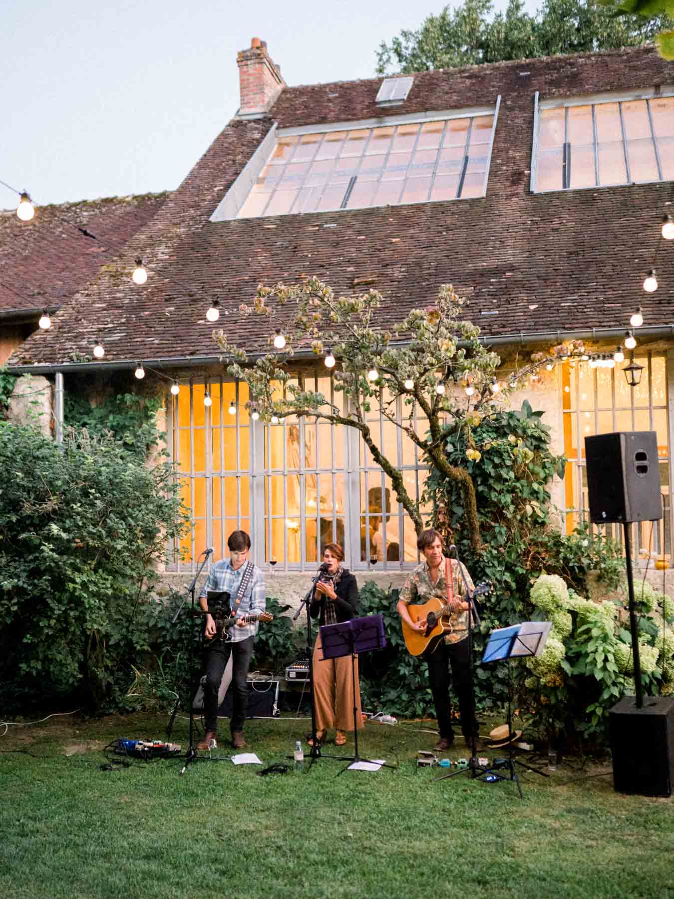 Band playing on the lawn in front of the house lit with string lights