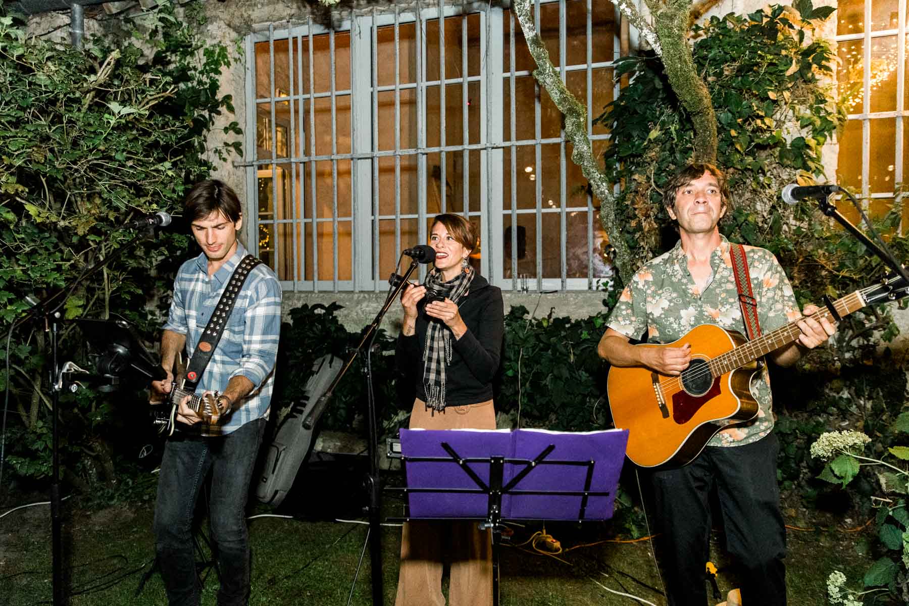 Acoustic trio performing in front of the house during the evening