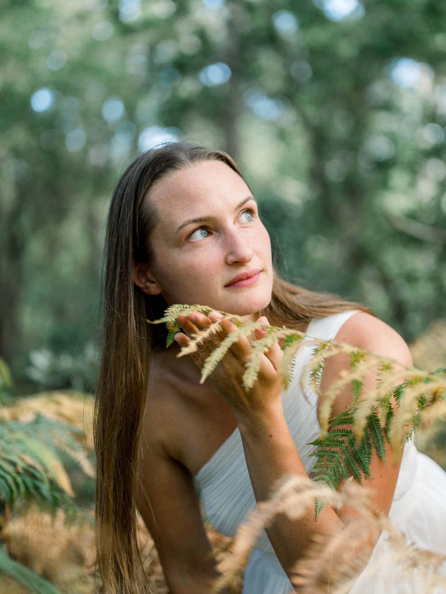 Young woman in a white dress lying among ferns, gazing upwards