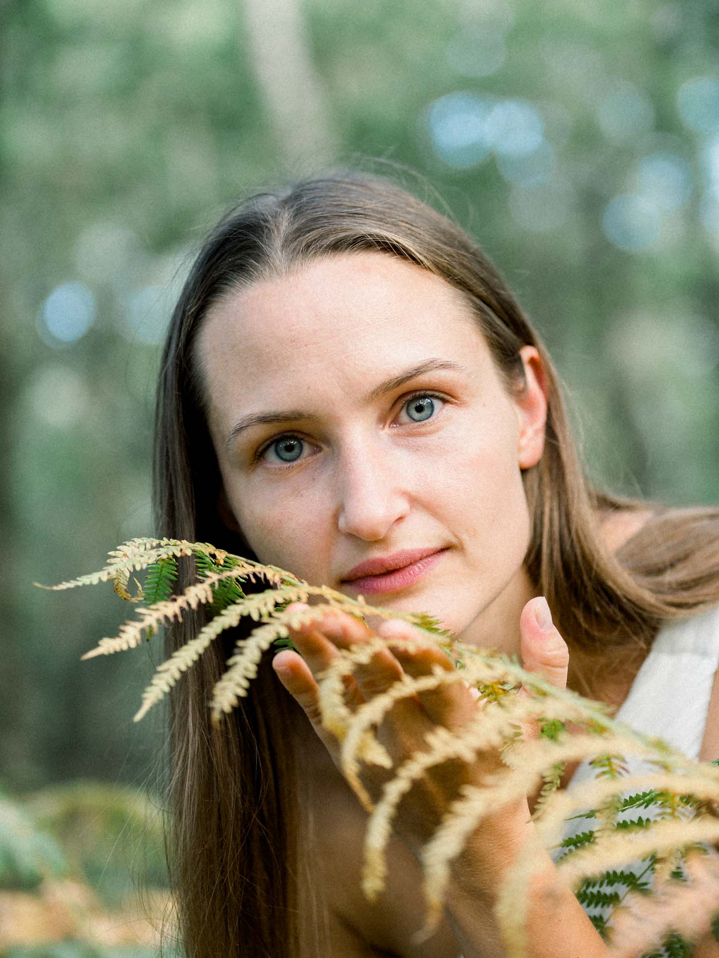 Portrait of a young woman with pale eyes holding a golden fern
