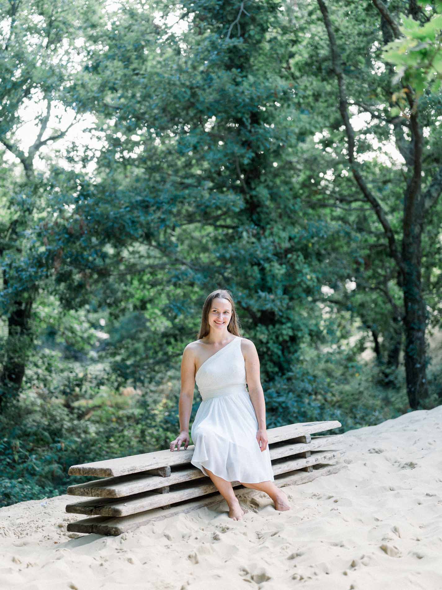 Young woman in a white dress seated on a wooden bench in the sand