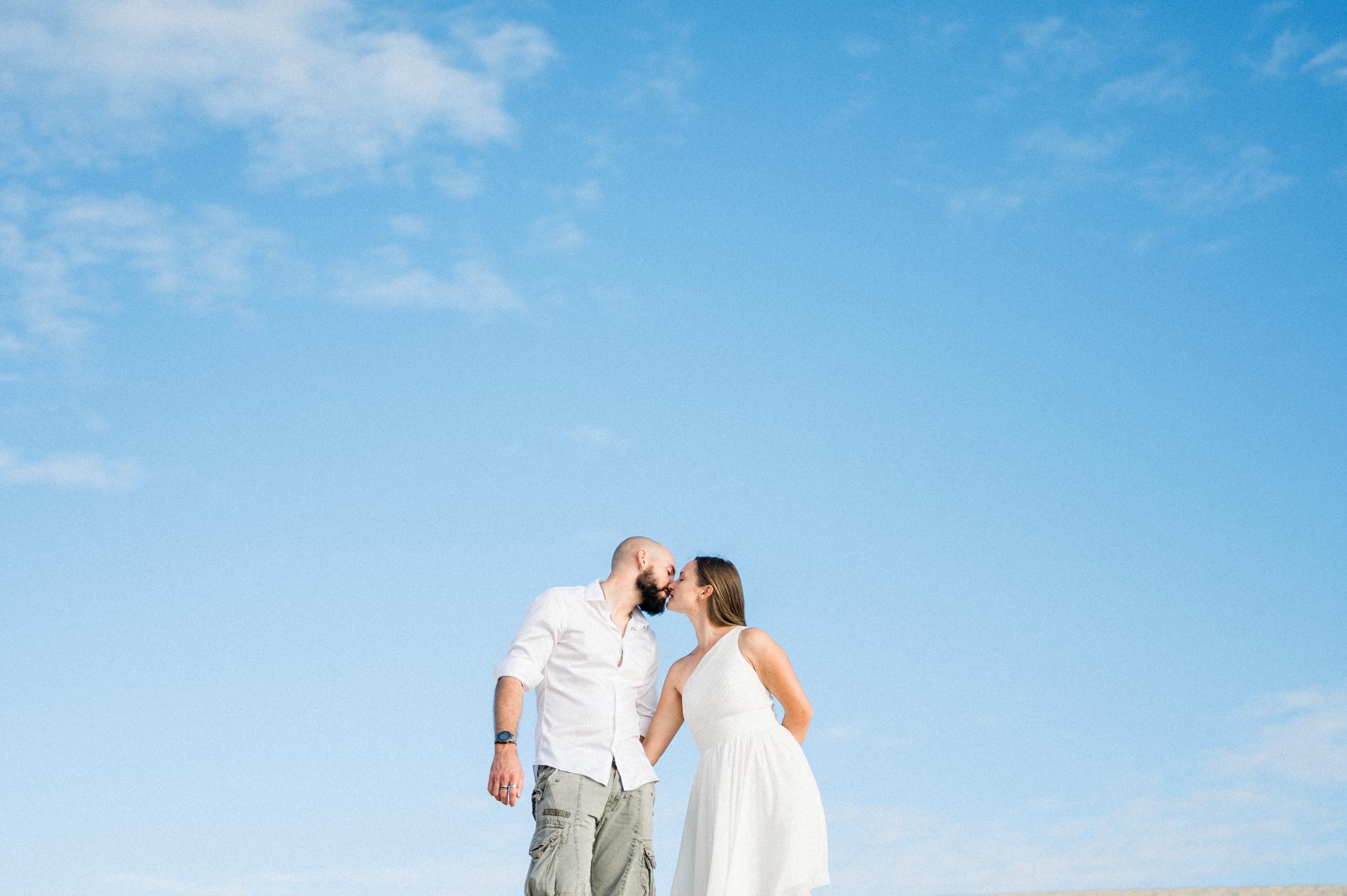 Couple kissing under a wide blue sky at the top of the dune