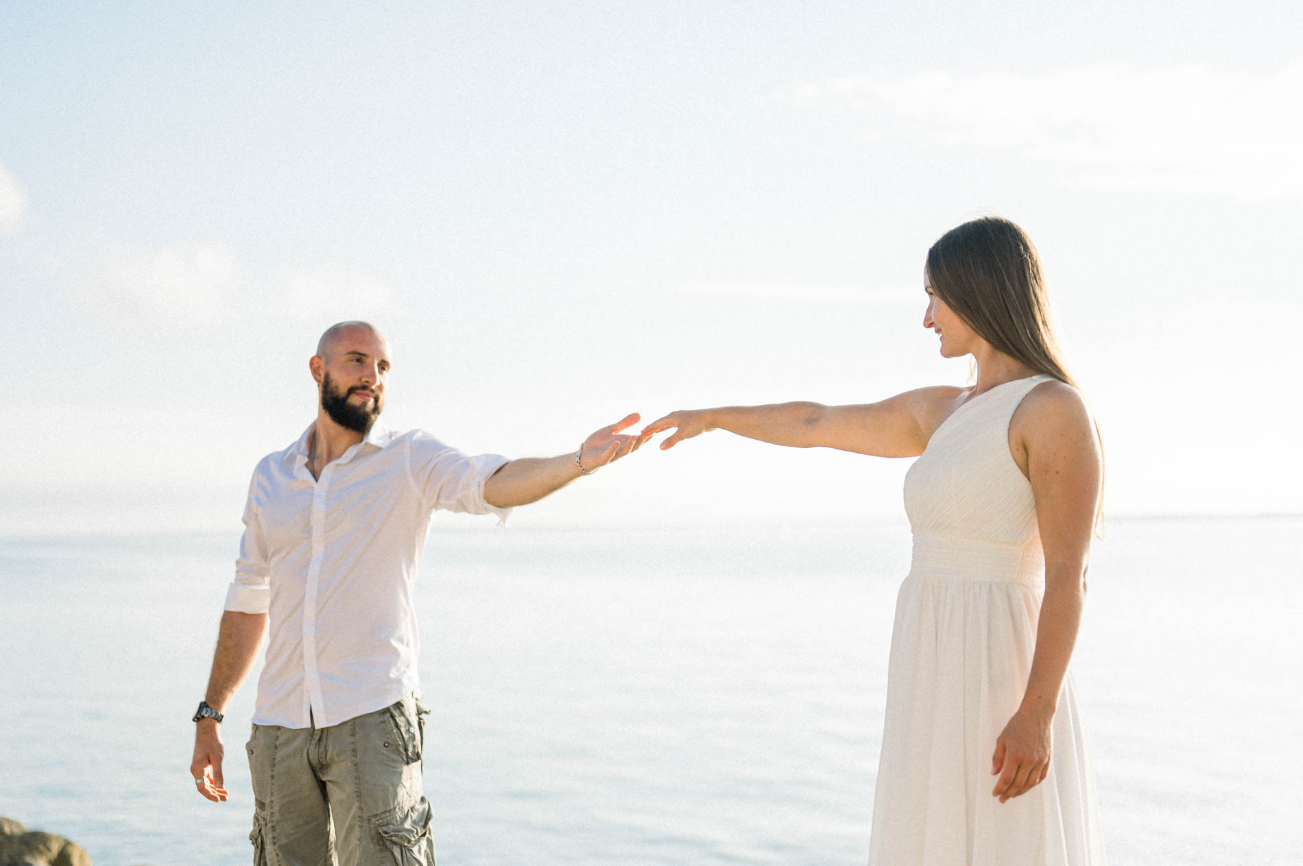 Couple reaching out their hands to each other at the water's edge