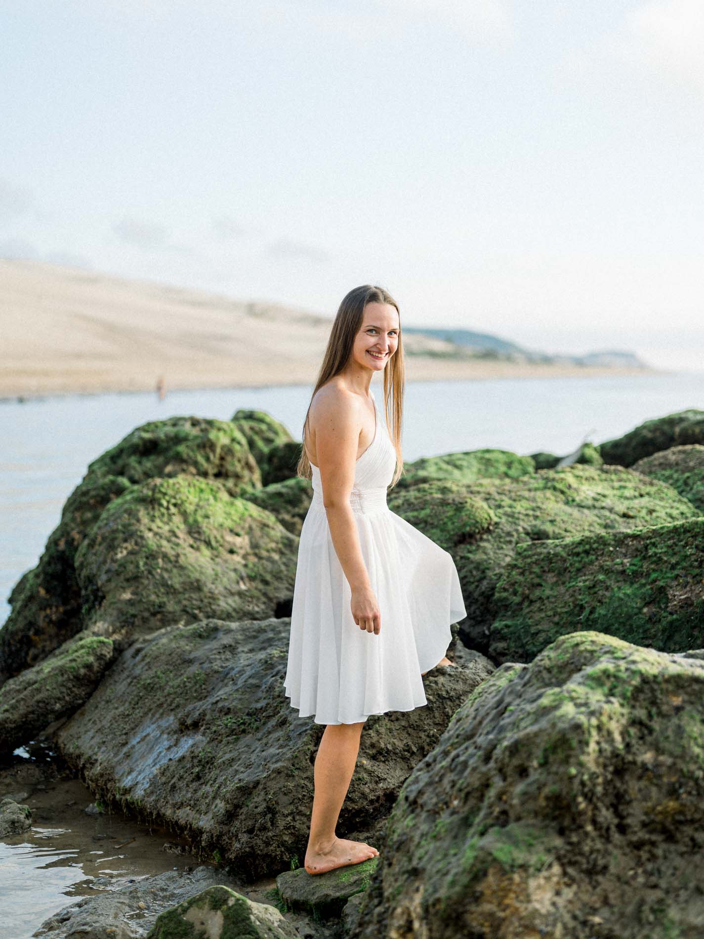 Smiling young woman standing on seaweed-covered rocks