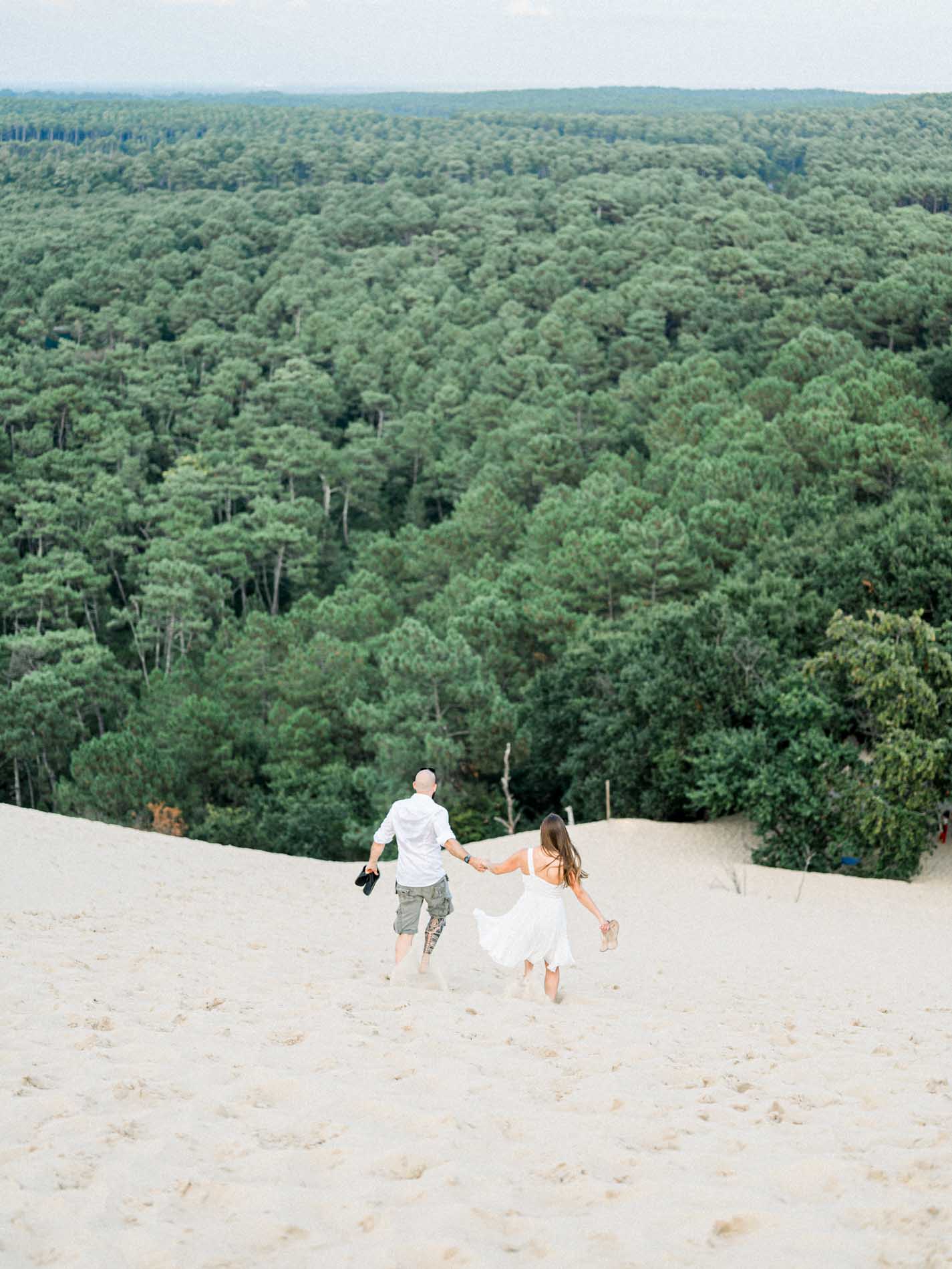Couple running hand in hand on the sand facing the forest