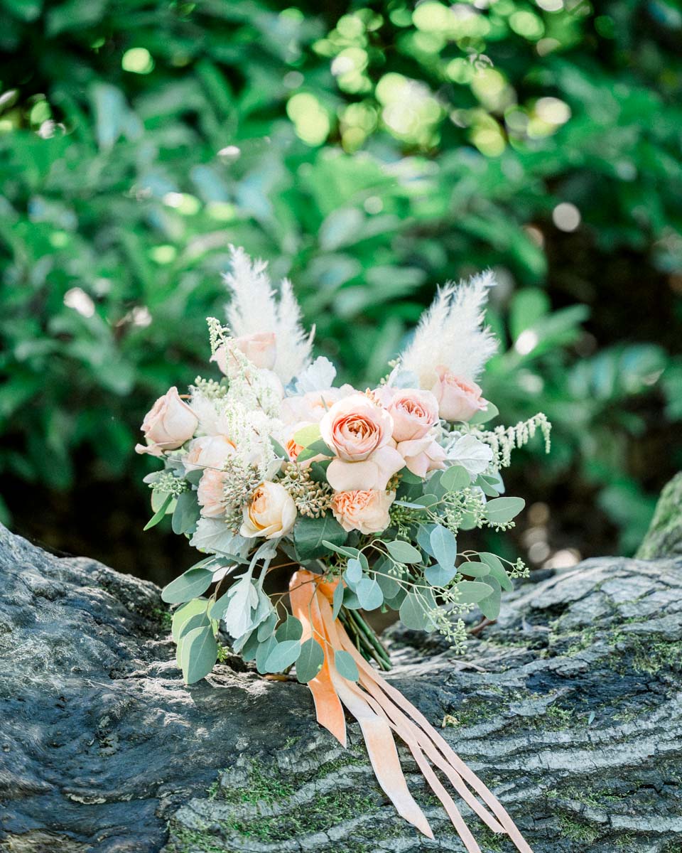 Bouquet of peach roses and pampas plumes resting on a log