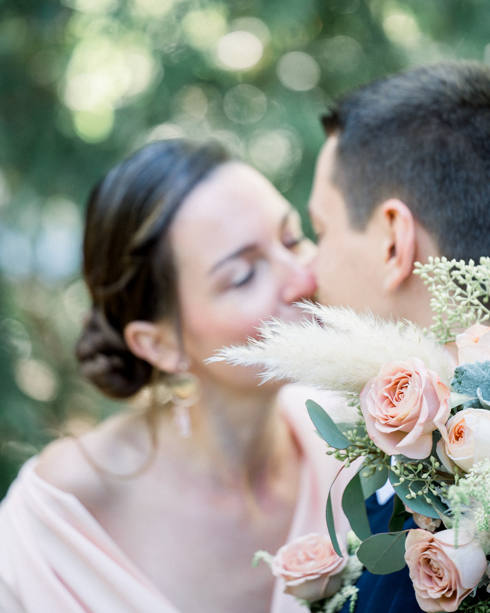 The couple cheek to cheek behind a bouquet of roses and pampas