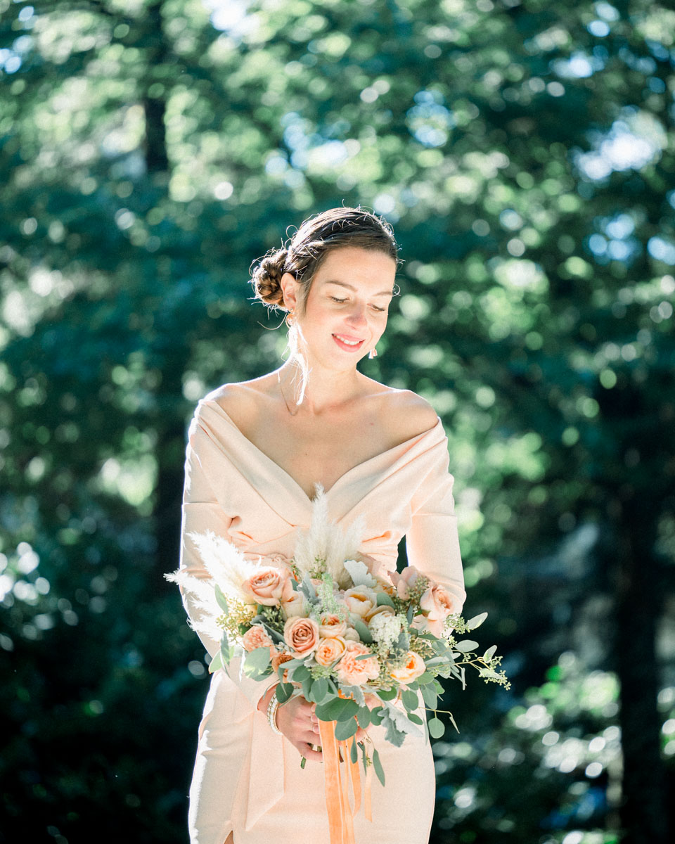 Young woman in a powder-pink dress holding her bouquet, eyes lowered