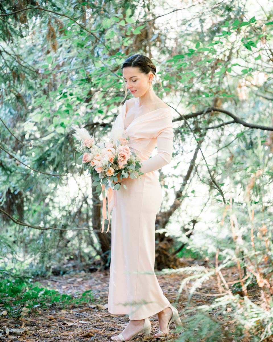 Young woman in a long pink dress among the park's shrubs