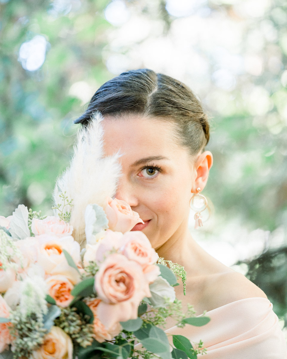 The young woman's gaze from behind her bouquet of peach roses