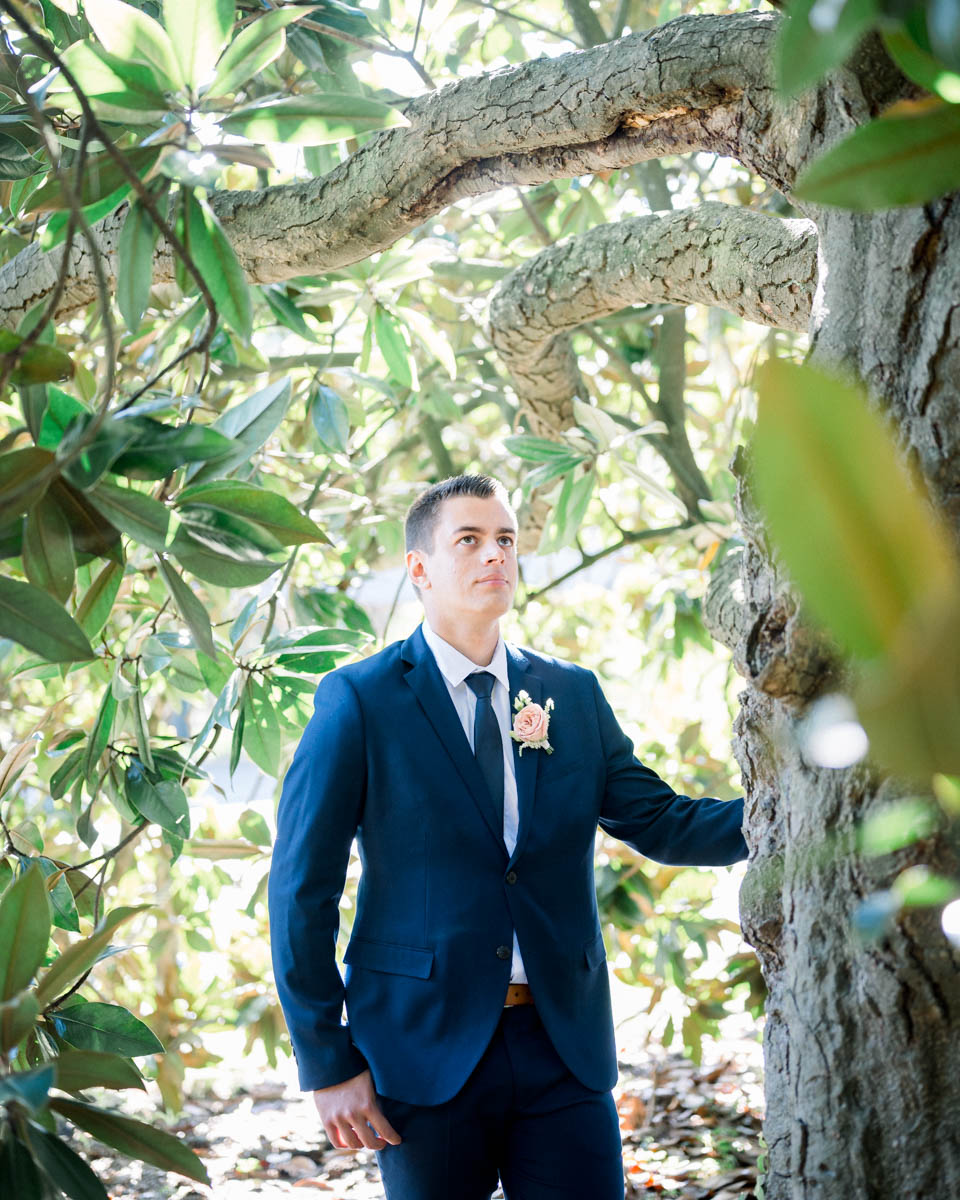 Man in a navy suit leaning against a tree in the park