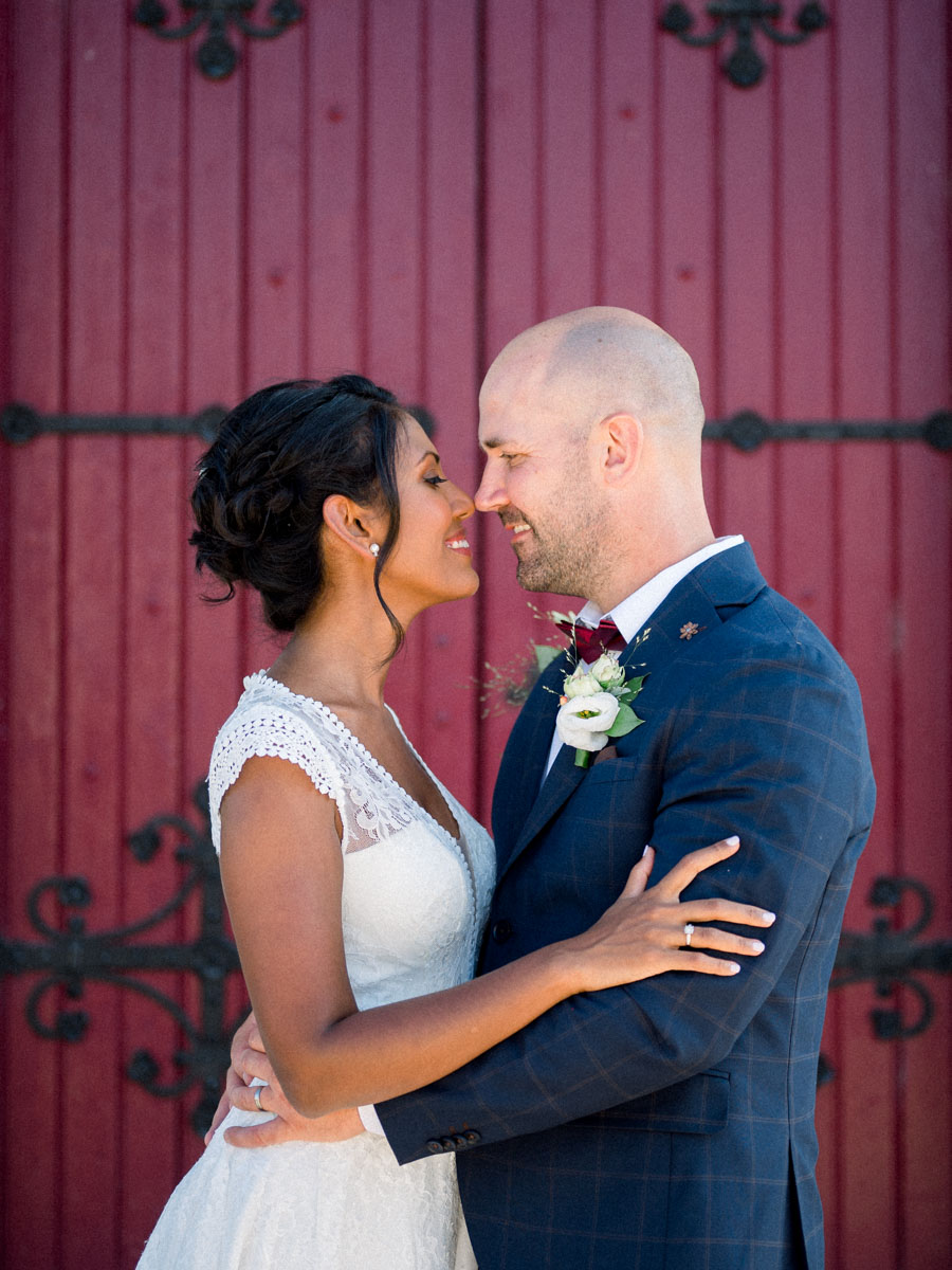 Meena and David embracing forehead to forehead before a large red door