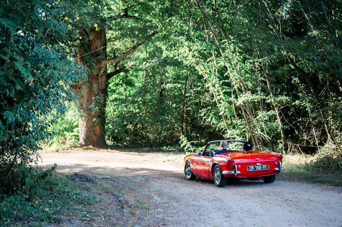 The couple's red convertible parked on a shady forest track