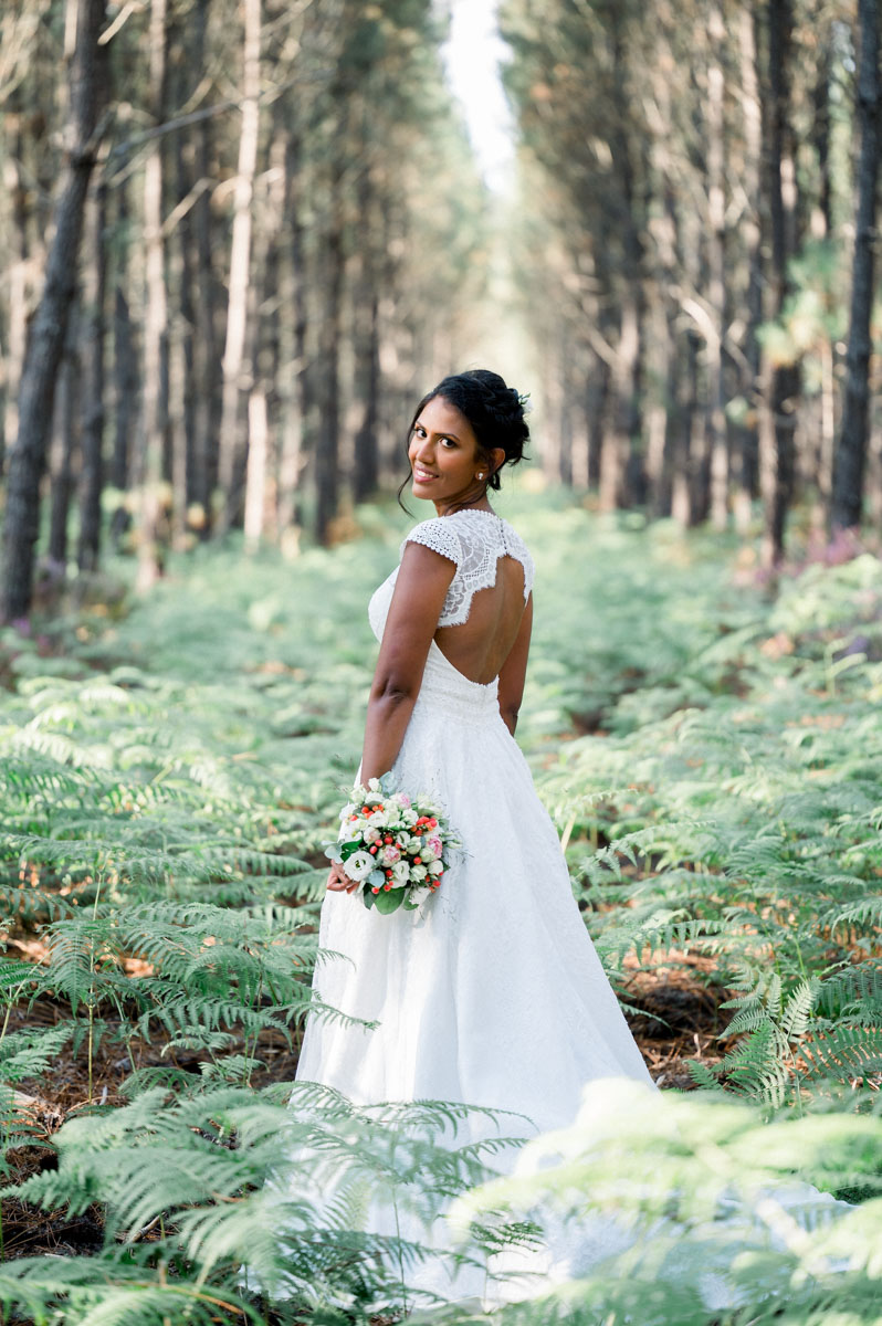 The bride from behind among the ferns of the pine forest, open-back gown