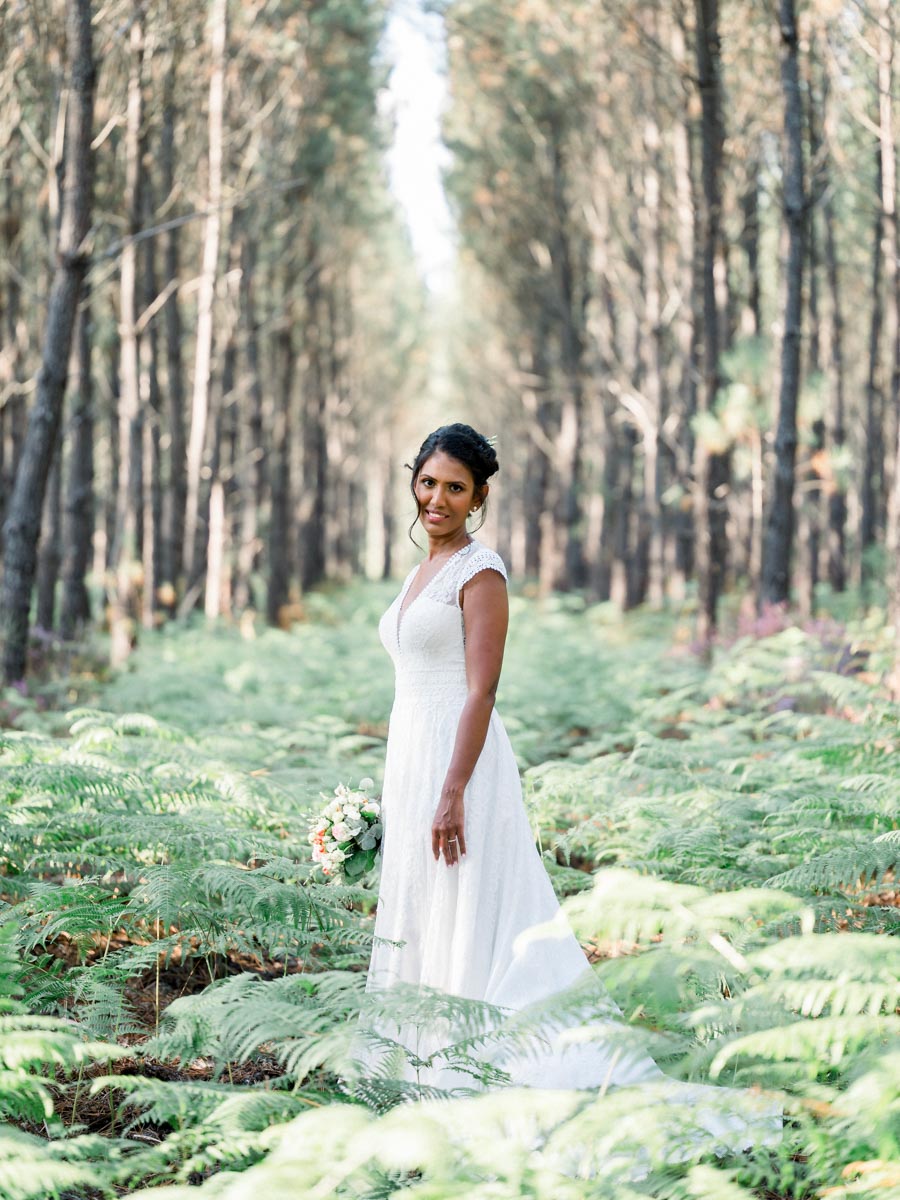 The bride standing amid the ferns between the tall pines of the Balizac forest