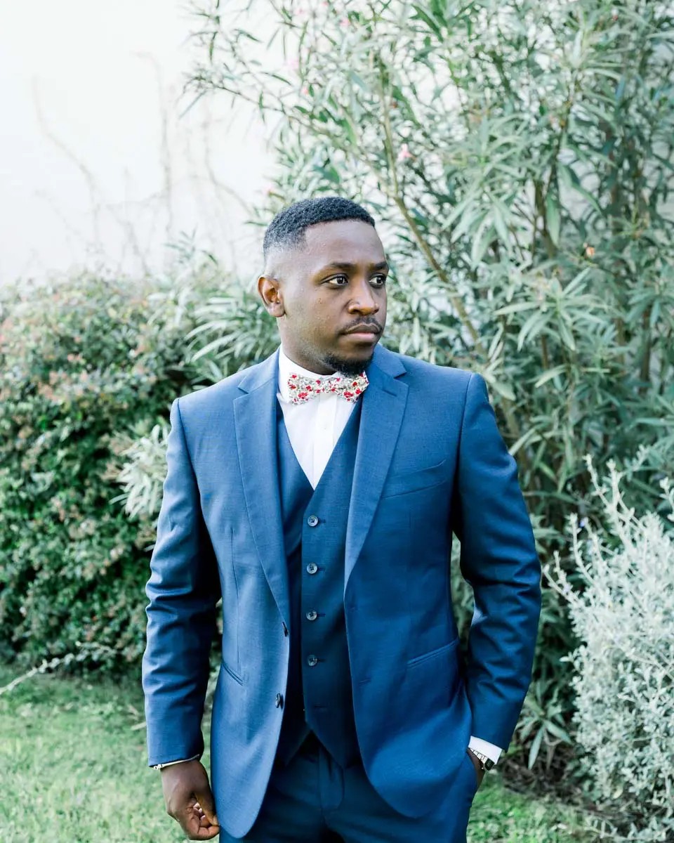 Groom in a blue three-piece suit and bow tie by an olive tree