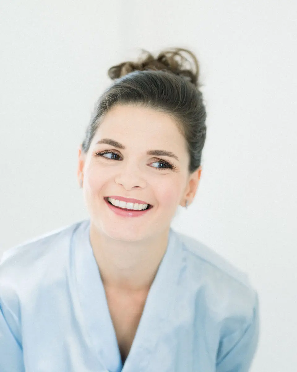 Claire smiling in a pale blue robe, hair in a bun, while getting ready