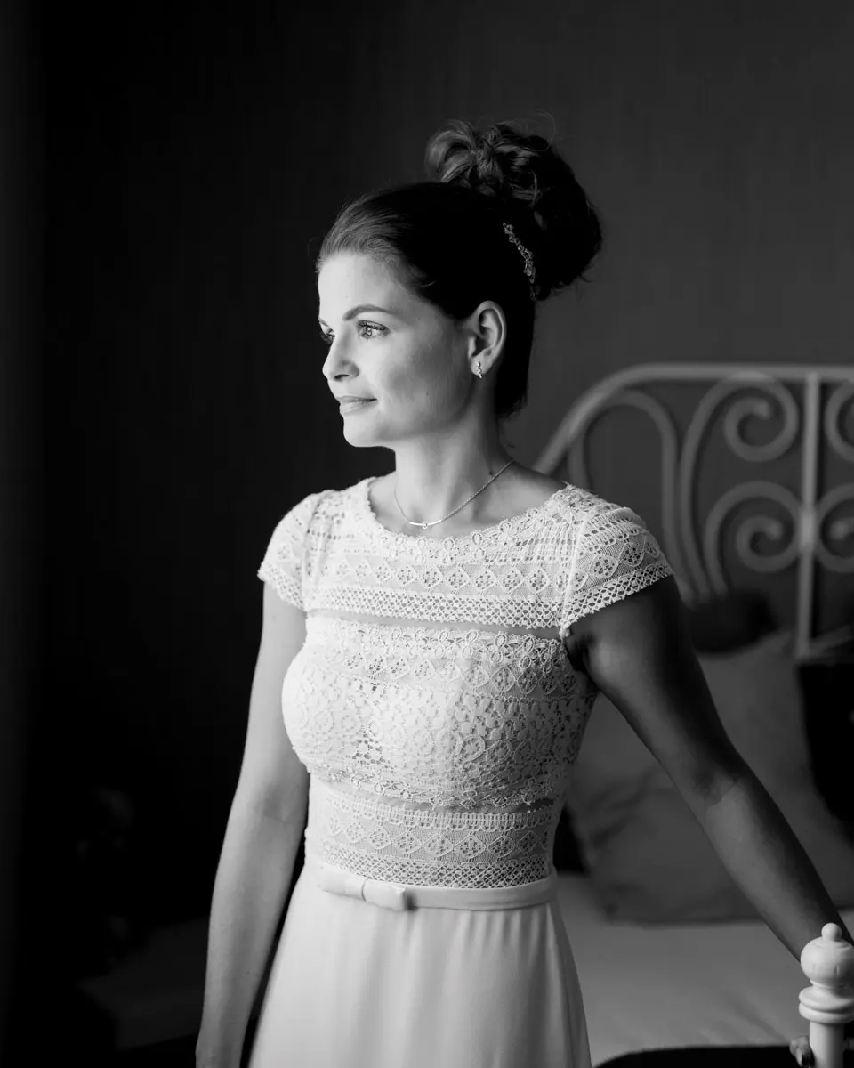 The bride in a lace gown by a wrought-iron bed, in black and white