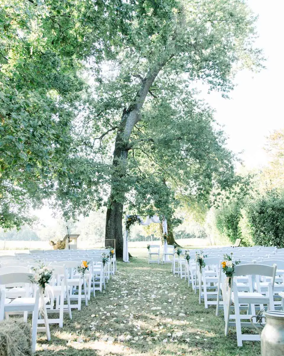 Aisle of white chairs decorated with flowers for the outdoor ceremony