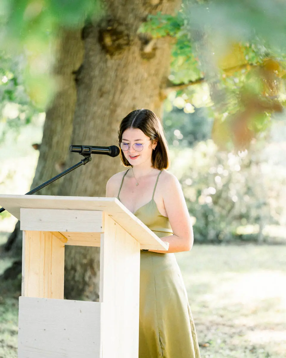 Guest in a green dress reading a speech at a wooden lectern